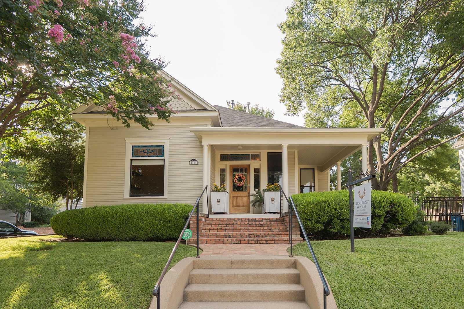 Historic house with porch and stairs, surrounded by trees and manicured lawn.